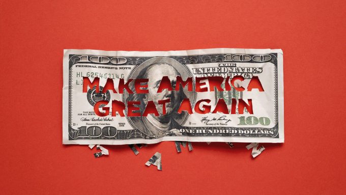 A $100 bill with 'MAKE AMERICA GREAT AGAIN' cut out of it, placed on a red background with letter fragments scattered below