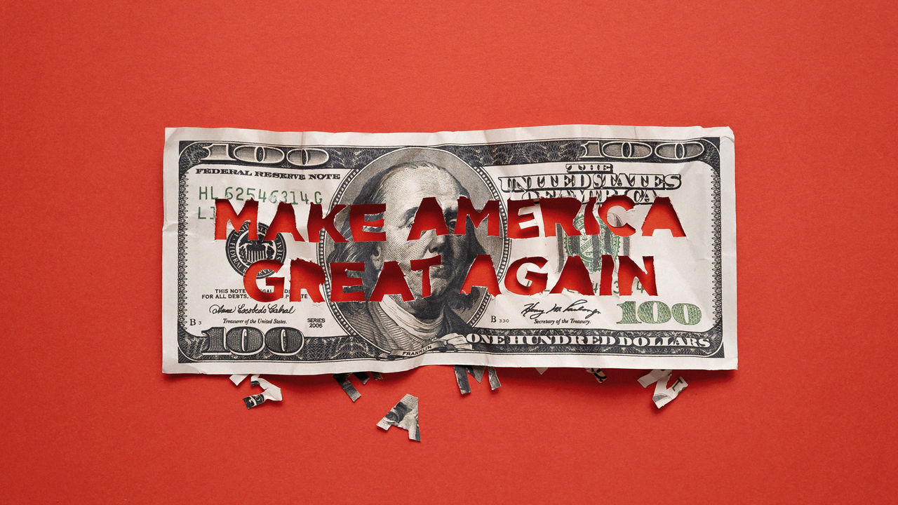 A $100 bill with 'MAKE AMERICA GREAT AGAIN' cut out of it, placed on a red background with letter fragments scattered below