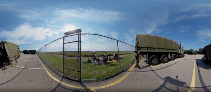 A distorted image of military vehicles in a parking lot next to a fence.