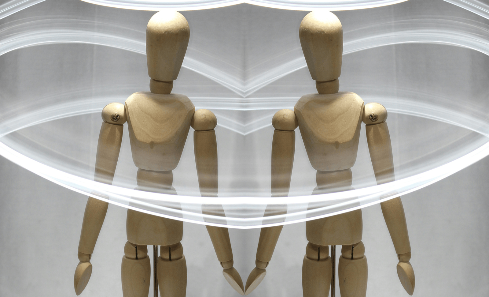 wooden artist's mannequin surrounded by trails of light. The photo is mirrored to create the two mannequins with their hands touching.