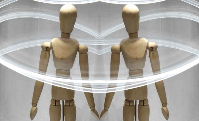 wooden artist's mannequin surrounded by trails of light. The photo is mirrored to create the two mannequins with their hands touching.