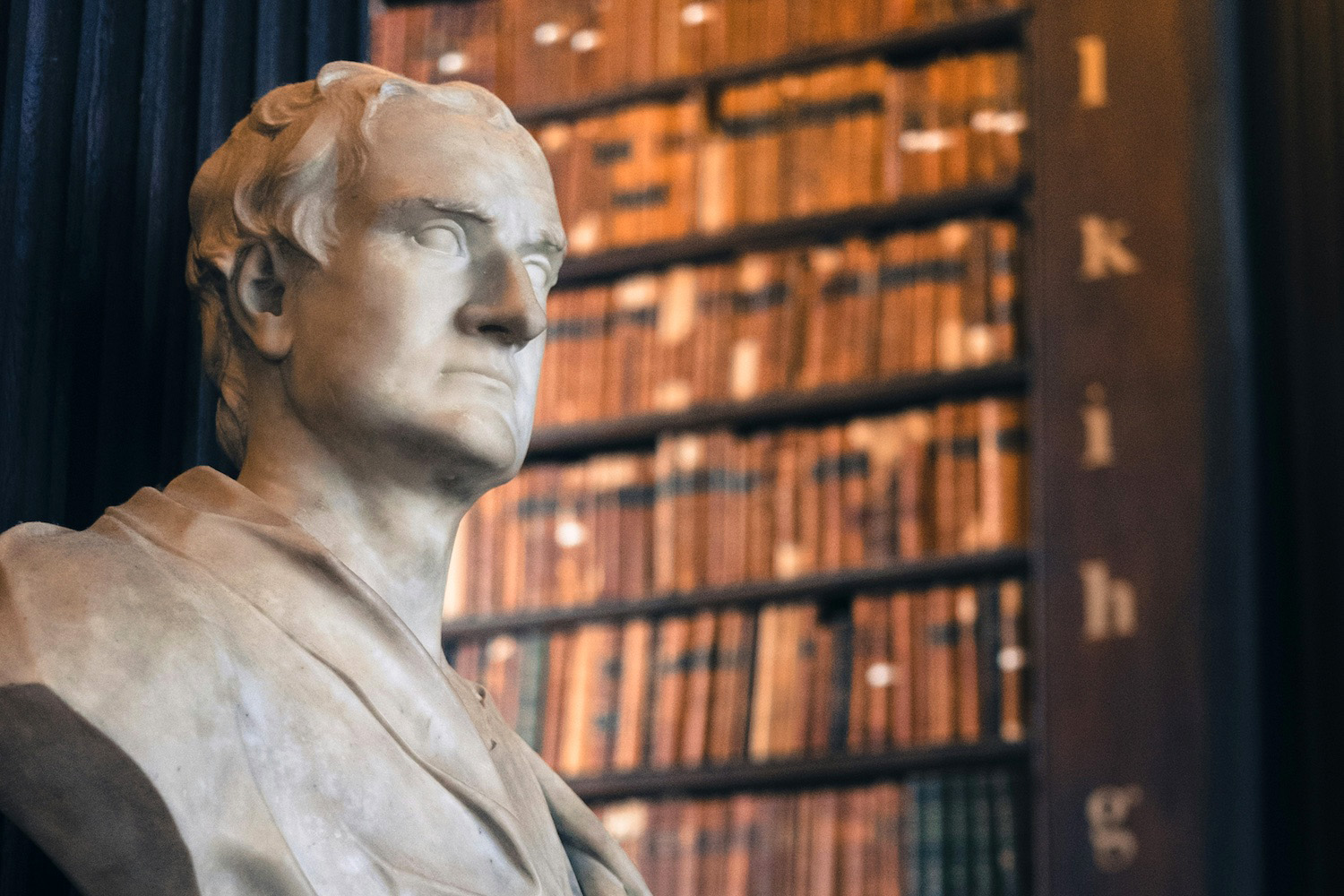 Photo of a bust of Isaac Newton in front of bookshelves at Trinity Library
